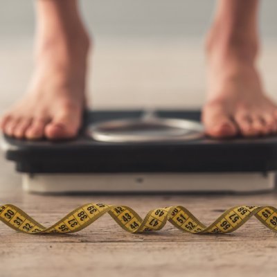 Man with feet on scale with tape measure in front.